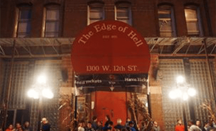 "The Edge of Hell haunted house entrance, featuring a large red sign at night, with a crowd gathered outside."