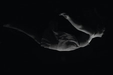 A black and white image of a person submerged in water, gracefully swimming with arms extended and body positioned sideways against a dark background.
